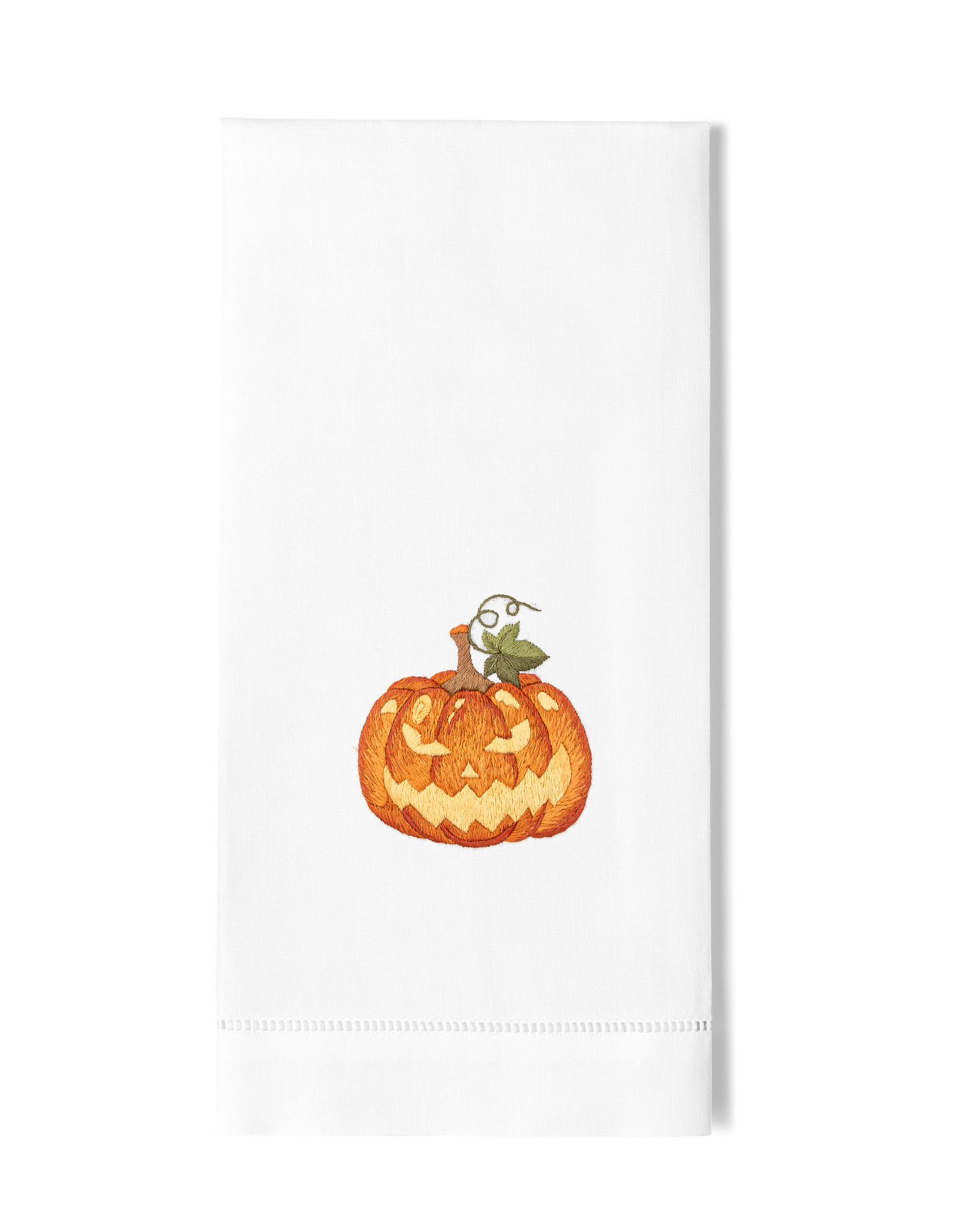 A white hand towel with a hemstitch. A jack o lantern is embroidered in the center.
